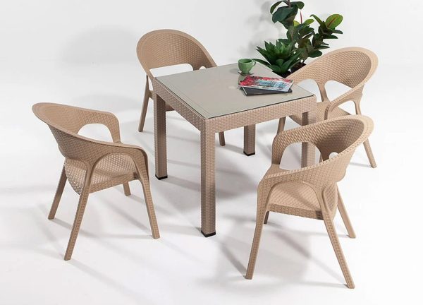 Black rattan-style outdoor dining set with four chairs and a square table, featuring a magazine and a potted plant on top, against a white background.